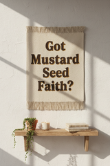Mustard Seed Faith tapestry hung on white wall styled with wooden shelf, trailing plant, candle and books in warm afternoon light